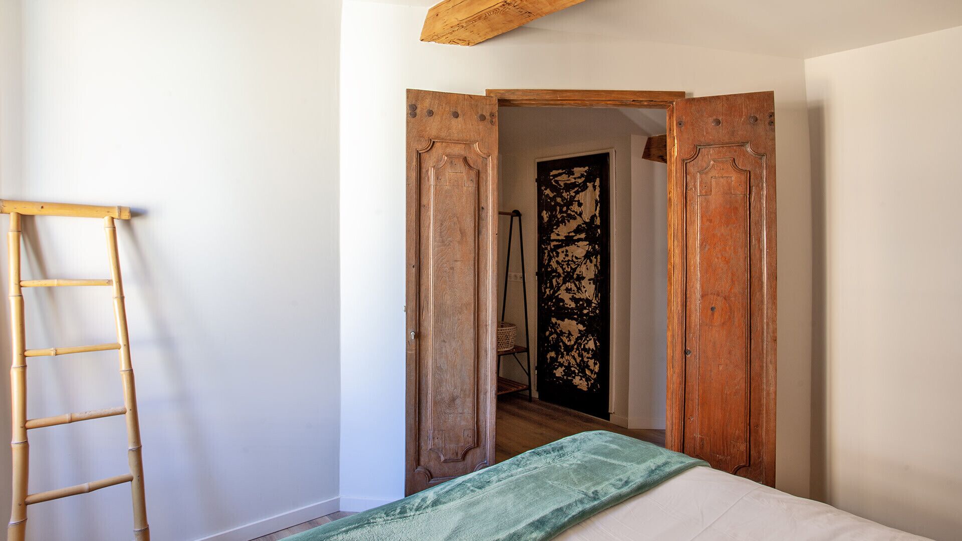 Une pièce avec un lit, une échelle en bois et une porte donnant sur une autre pièce.