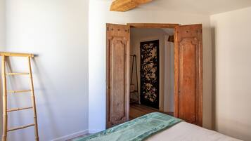 Une pièce avec un lit, une échelle en bois et une porte donnant sur une autre pièce.