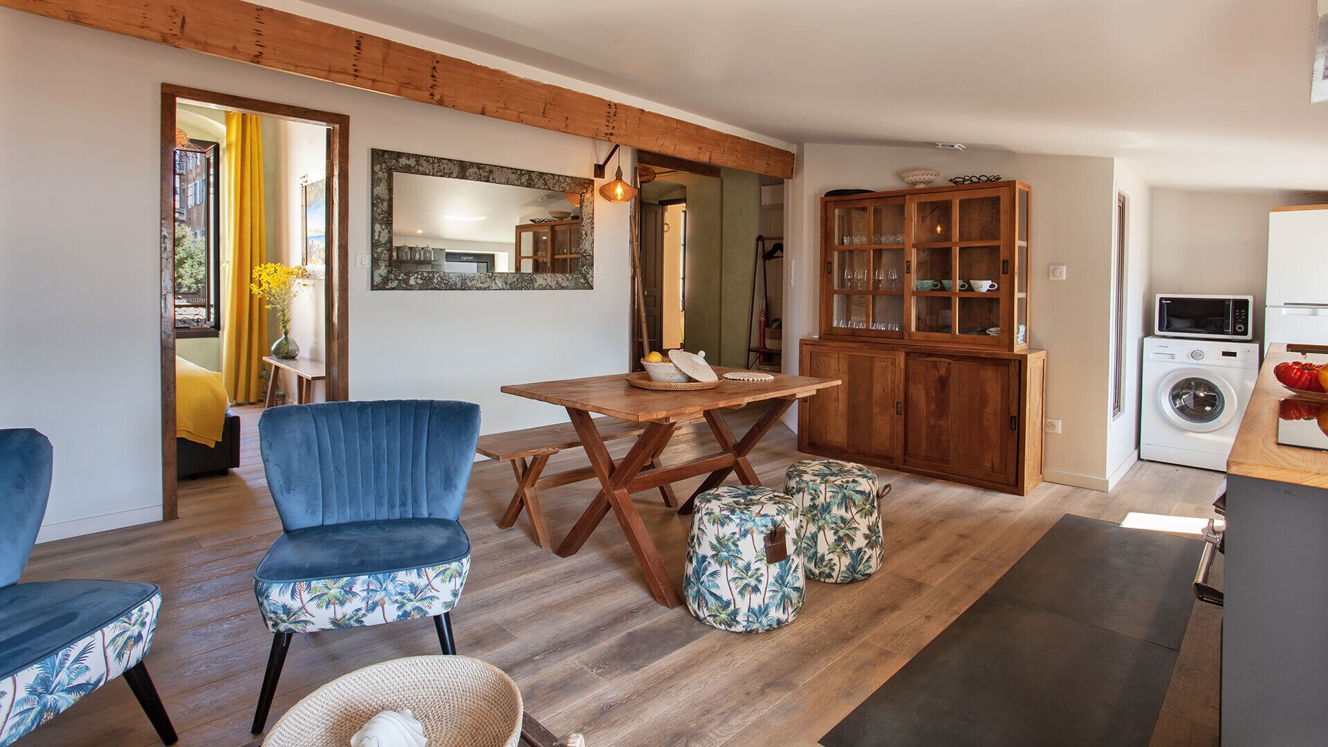 Un salon chaleureux avec une table à manger en bois, des chaises rembourrées bleues, un meuble avec des portes en verre et un lave-linge.