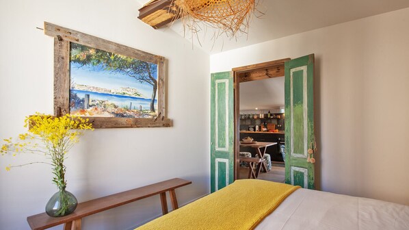 A bedroom with a bed, a bench, a painting, and a vase with flowers.