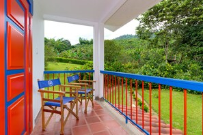 Un balcon avec des balustrades rouges, des chaises en bois et une vue sur un jardin luxuriant.