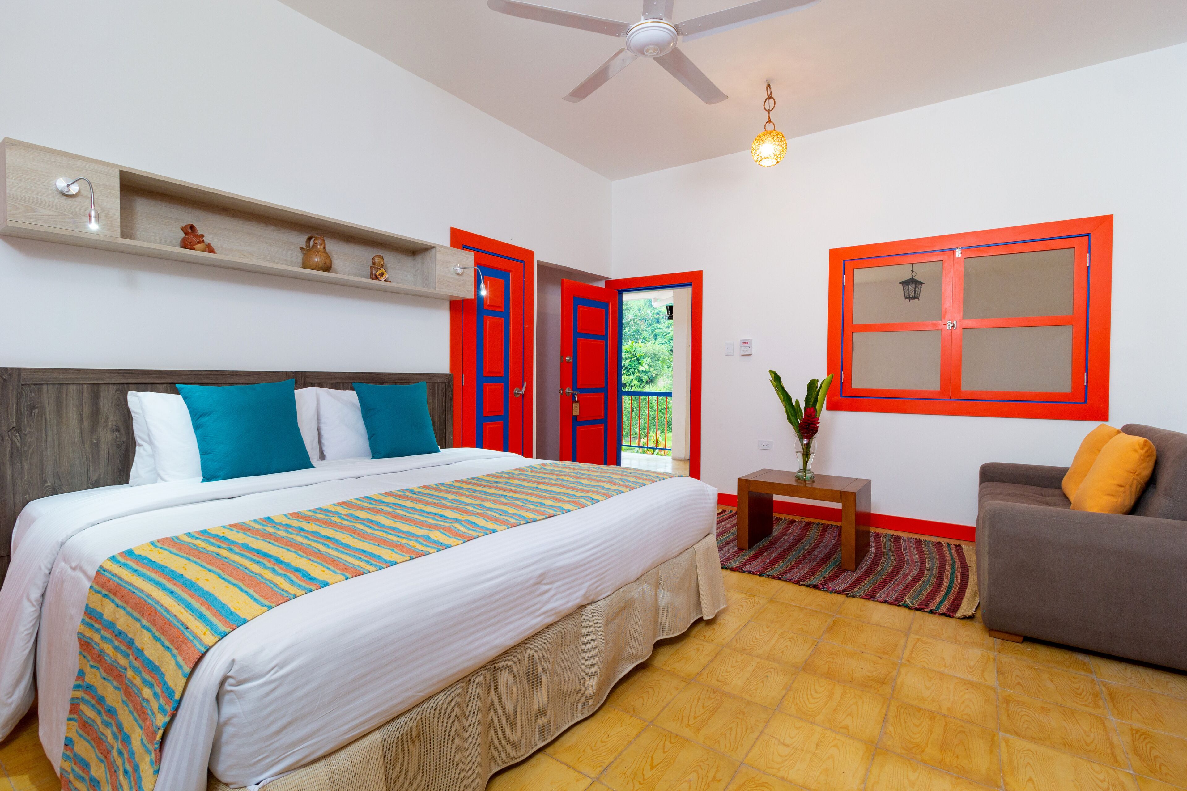 A bedroom with a bed, a bedside table, a chair, a ceiling fan, and a window with red frames.