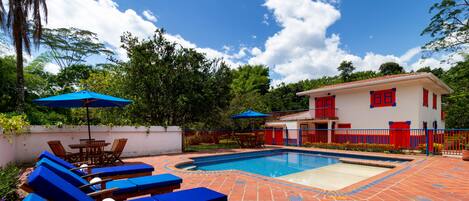 A pool area with blue lounge chairs and umbrellas, a tiled patio, and a building with red accents.