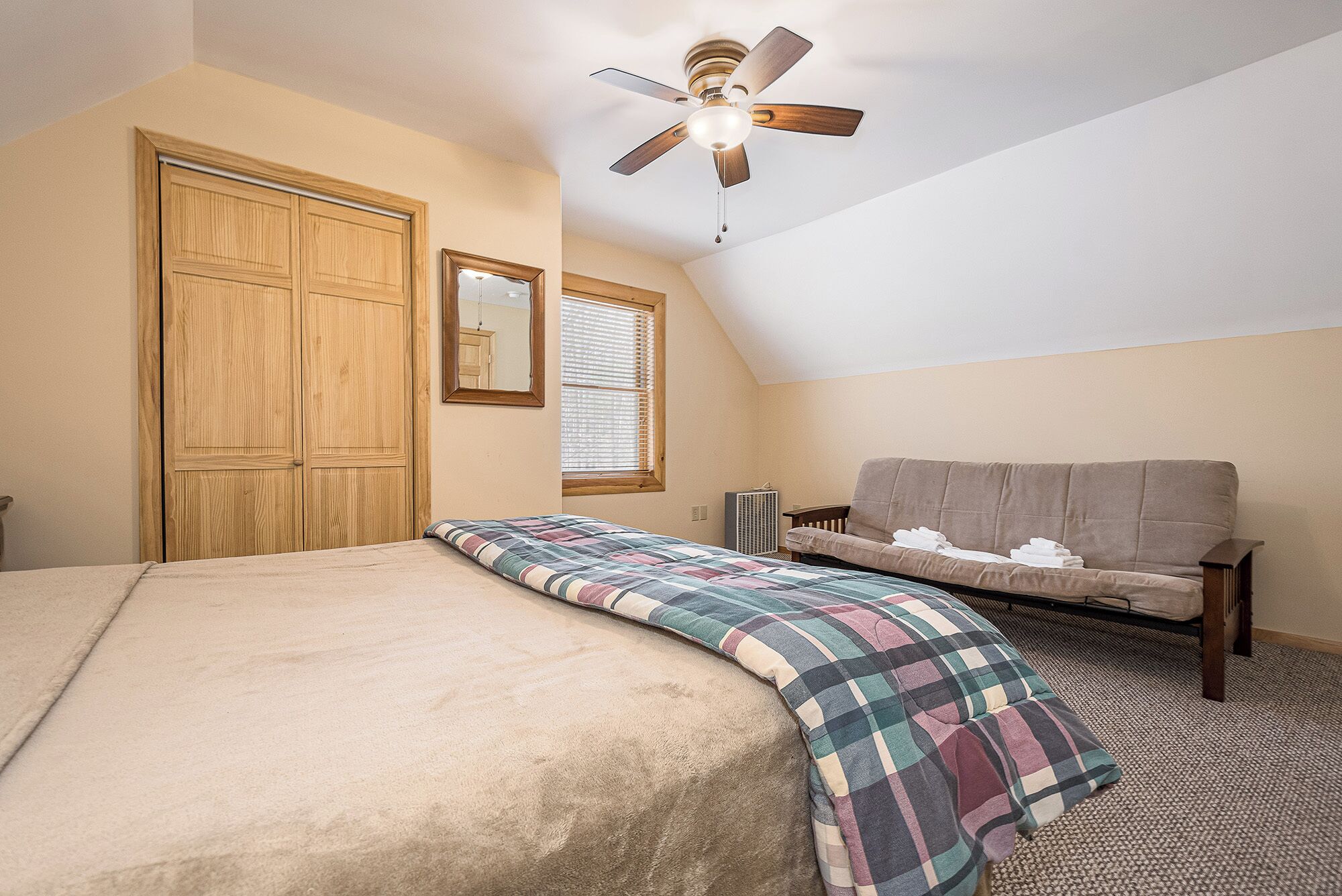 A bedroom with a bed, a sofa, a ceiling fan, a window with blinds, and a radiator.