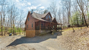 A log cabin with a porch and a chimney, surrounded by trees and a gravel driveway. - Crazy Idea by Taylor Made Deep Creek (McHenry)