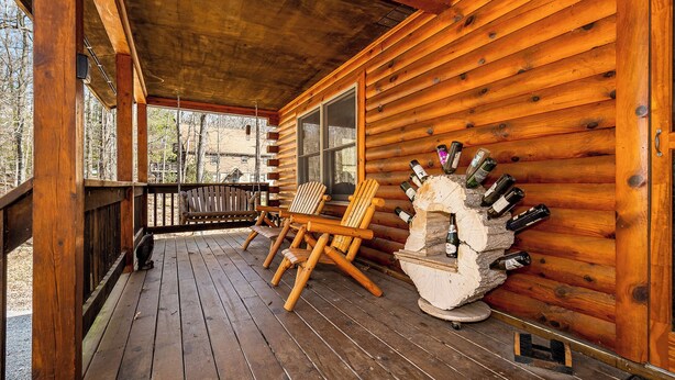 A wooden cabin with a porch, two Adirondack chairs, and a stone fireplace with wine bottles. - Crazy Idea by Taylor Made Deep Creek (McHenry)