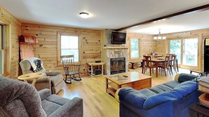 A cozy cabin-style room with a fireplace, wooden walls, a television, and a dining area. - Crazy Idea by Taylor Made Deep Creek (McHenry)
