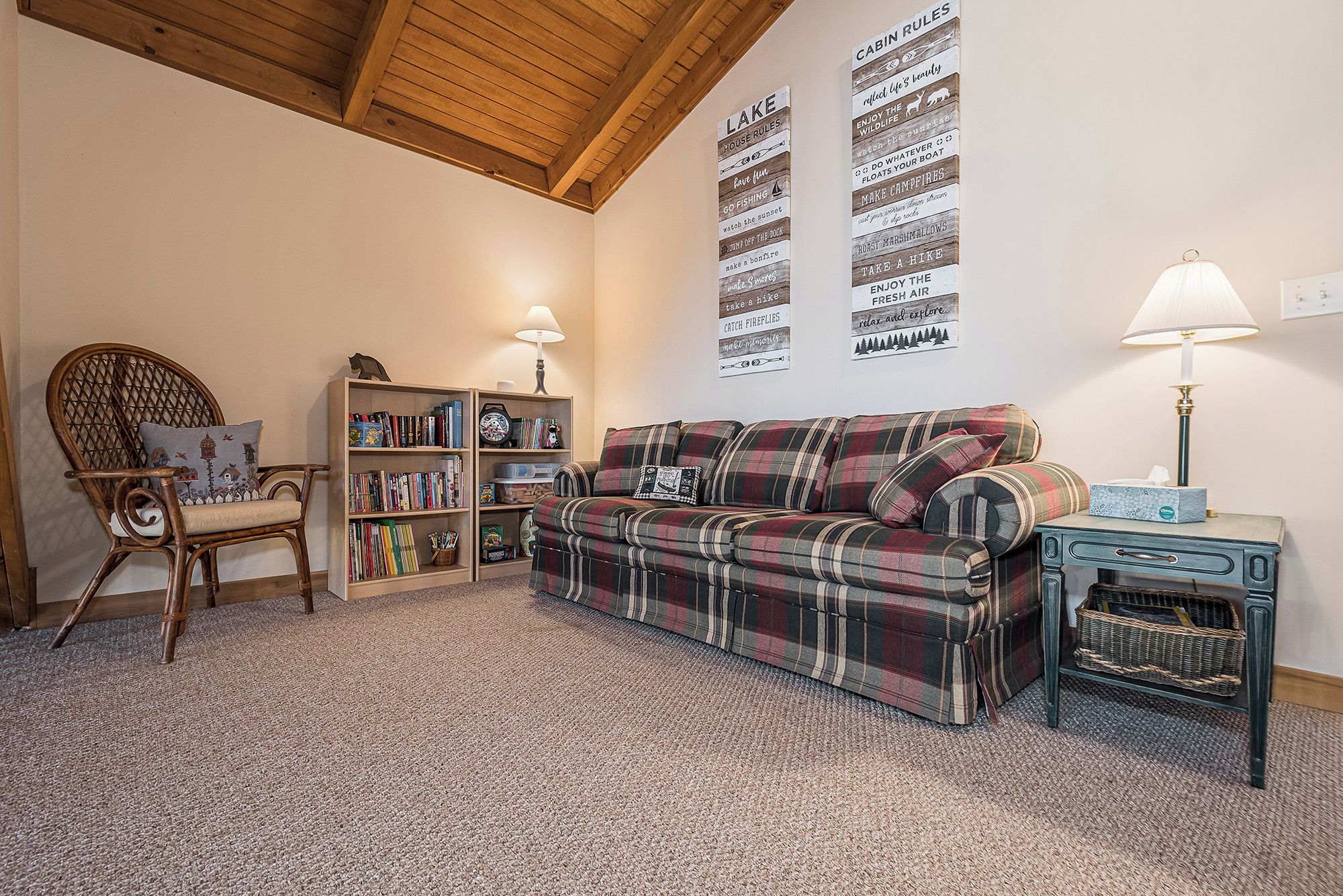 A cozy living room with a plaid sofa, a wooden chair, a bookshelf, and a lamp.