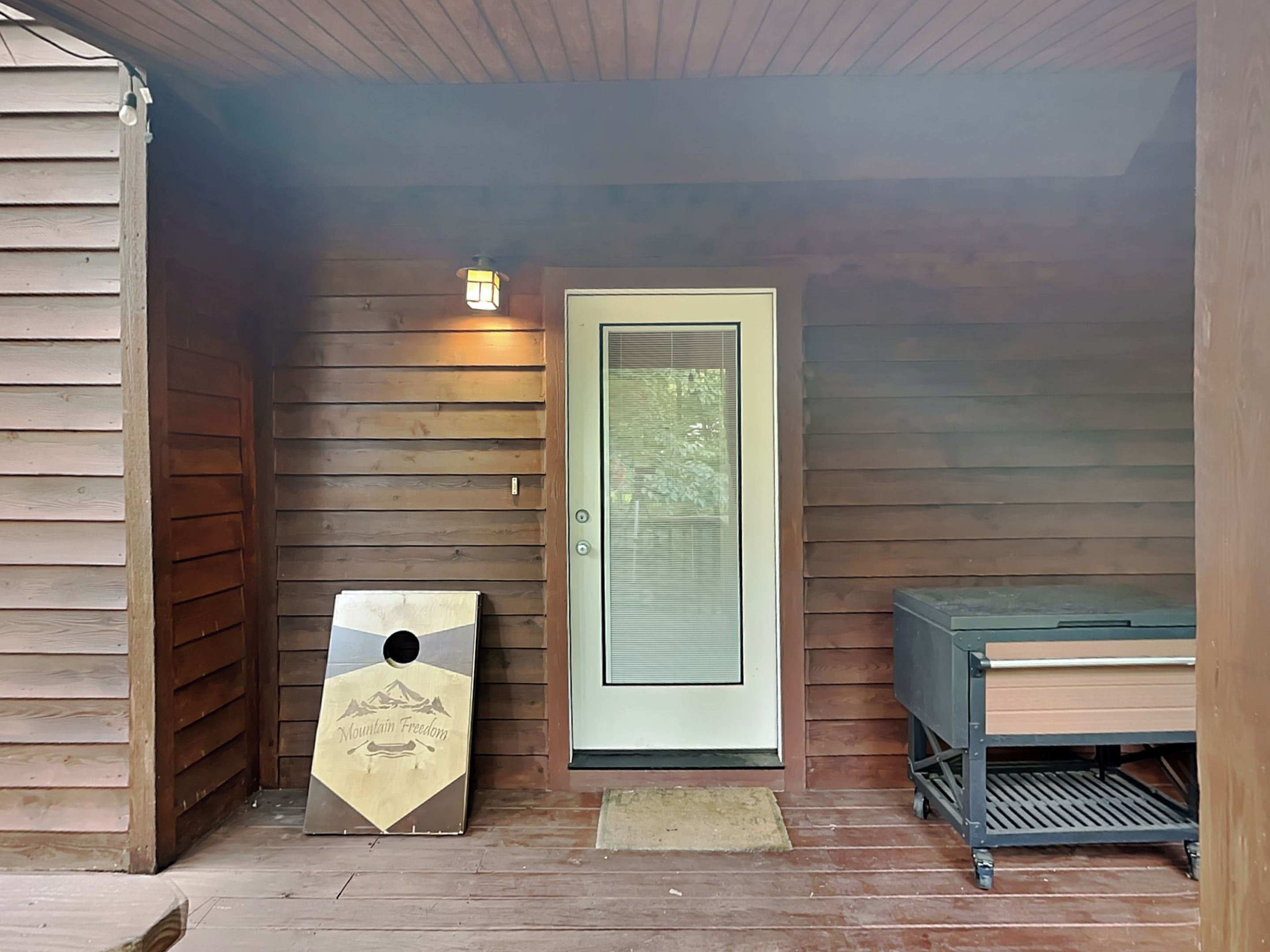 Eingang eines Holzchalets mit Tür, einem kleinen Tisch und einem Metallgrill.