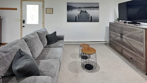 A living room with a grey sofa, a coffee table, a TV, and a painting of a pier. - Mountain Freedom by Taylor Made Deep Creek (Oakland)