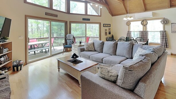 A spacious living room with a large gray sectional sofa, wooden flooring, and a high ceiling with exposed beams. - Mountain Freedom by Taylor Made Deep Creek (Oakland)