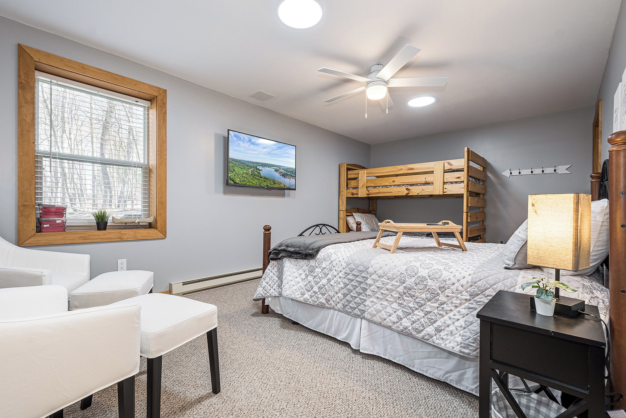 Une chambre avec un lit superposé, un bureau, une chaise, un ventilateur de plafond et une fenêtre avec des stores.