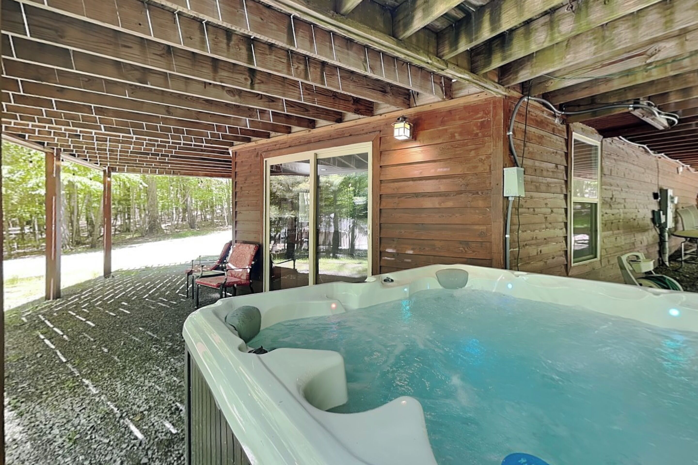 Ein Whirlpool in einem überdachten Außenbereich mit Ziegelboden, Holzvertäfelung und Blick auf einen Garten.