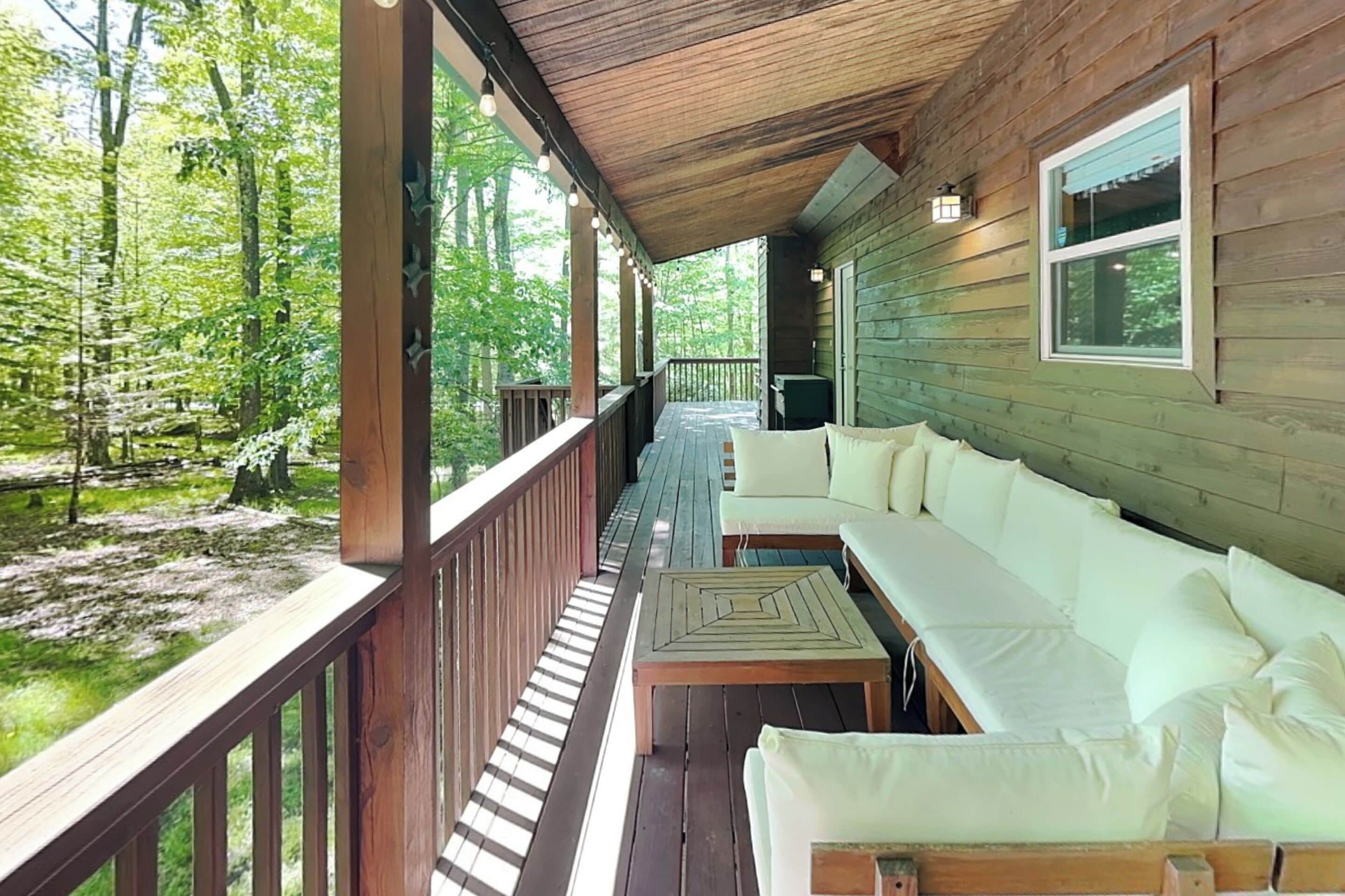 A wooden deck with a sofa and a table, surrounded by a forest.