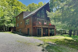 A two-story wooden cabin with a balcony, surrounded by trees.