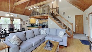 A spacious living area with a large grey sectional sofa, a wooden coffee table, and a kitchen in the background. - Mountain Freedom by Taylor Made Deep Creek (Oakland)