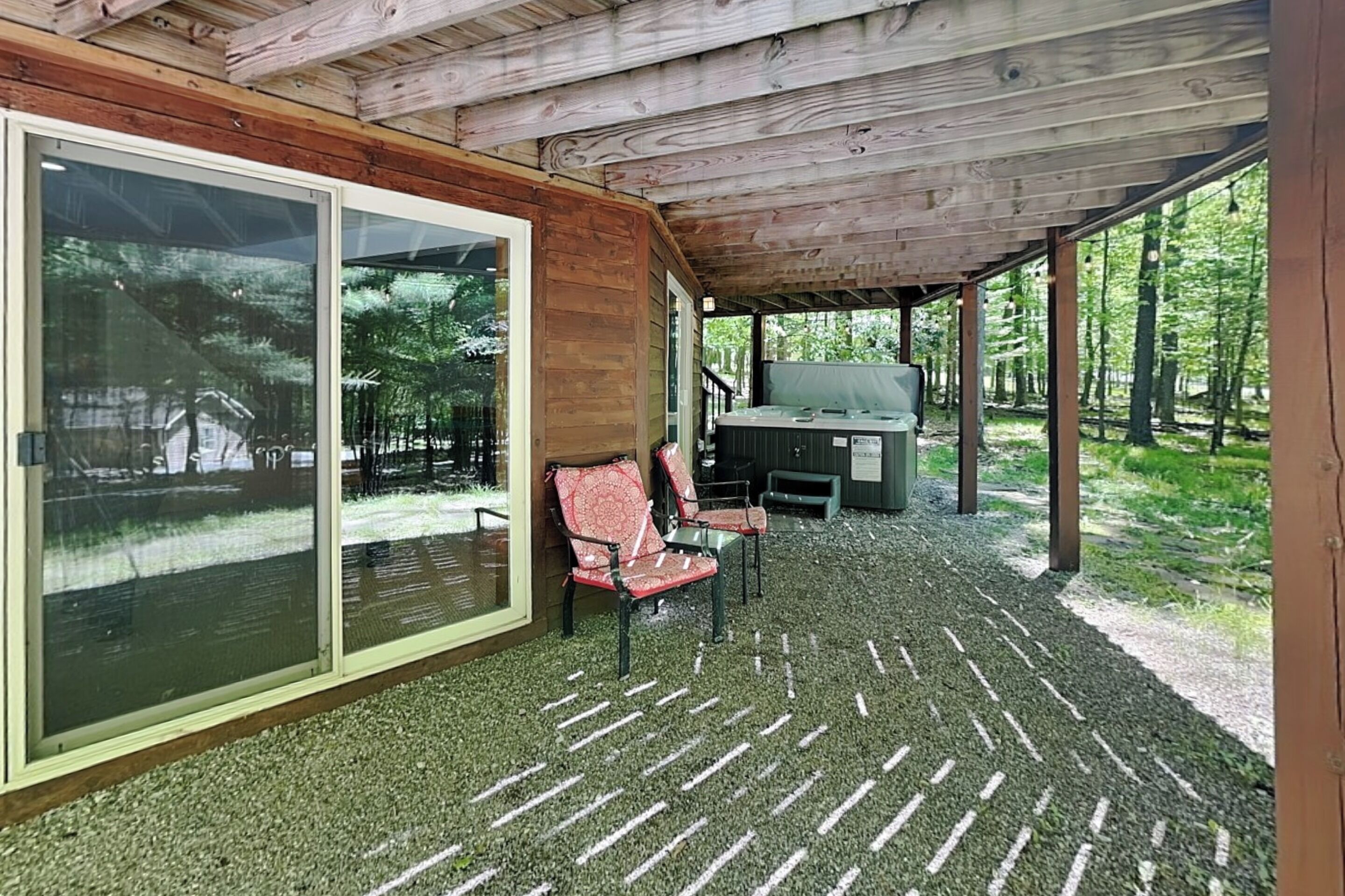 A covered outdoor area with a seating arrangement, a grill, and a view of the surrounding forest.
