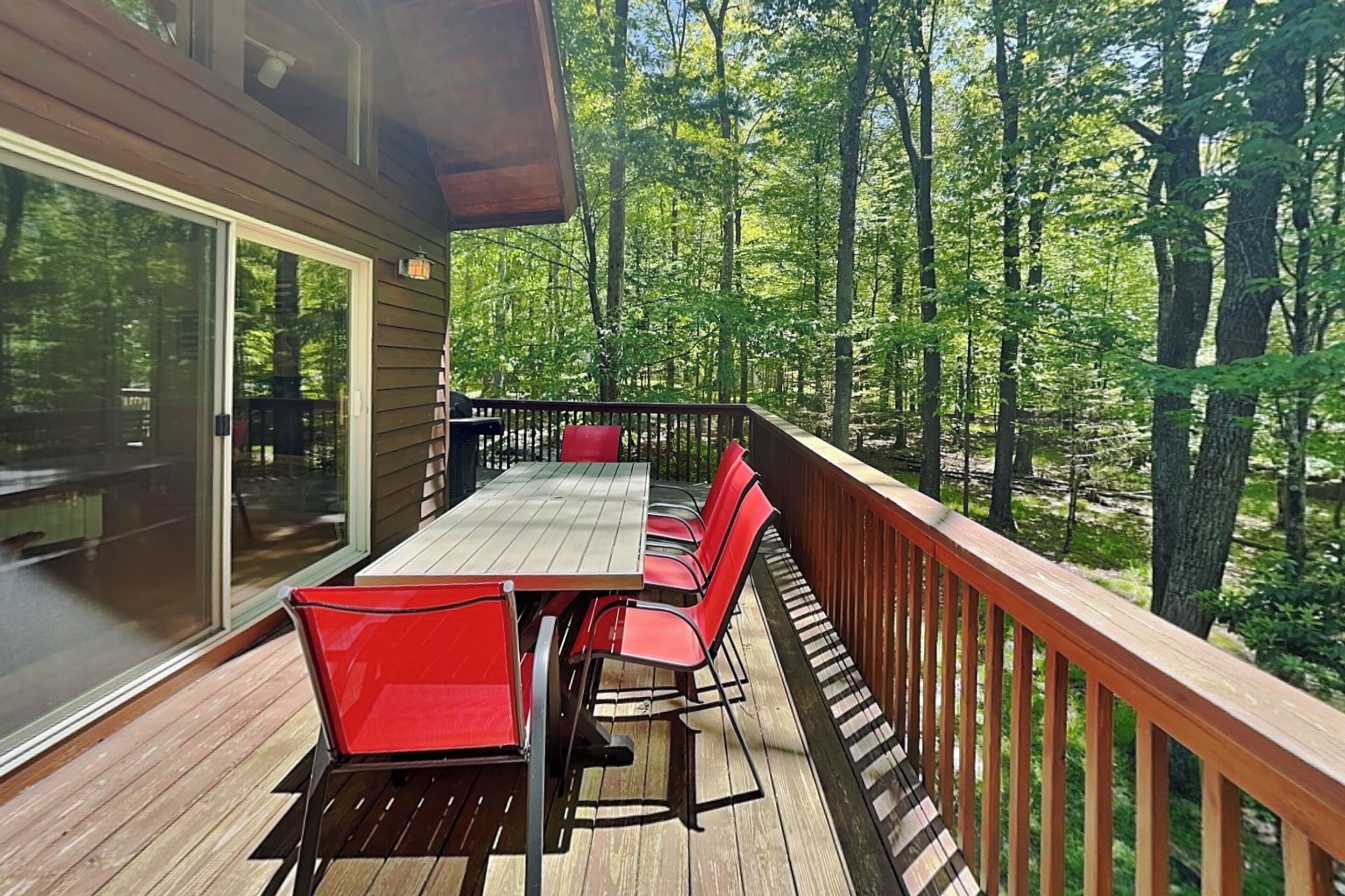 A wooden deck with a table and chairs, surrounded by a forest.
