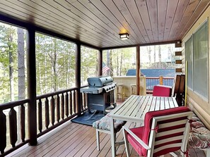 A covered deck with a grill, a table, and two chairs.