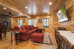 A log cabin interior with a red sectional sofa, a dining table, and a fireplace.