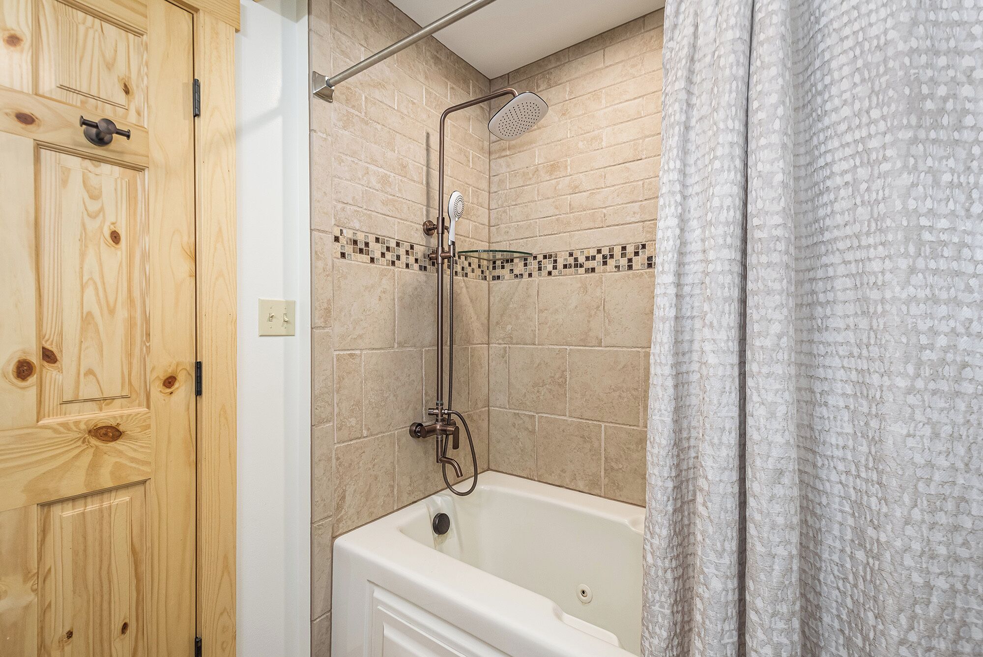 A bathroom with a bathtub, a shower with a glass-enclosed showerhead, and a wooden door.