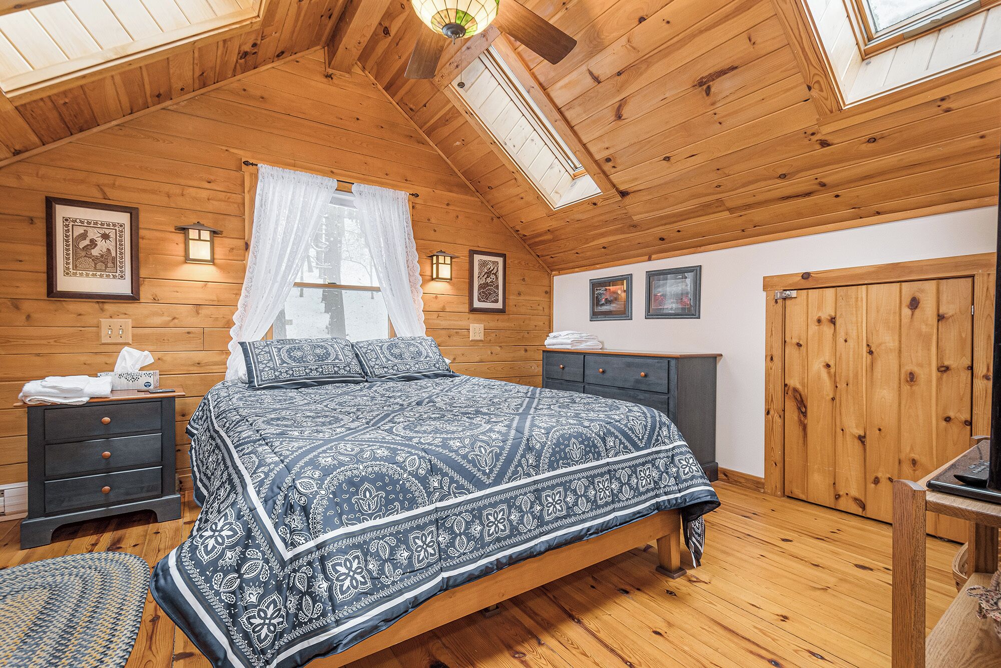 Une chambre confortable avec un plafond en bois, un lit recouvert d’une literie à motifs, une table de chevet, une commode et une armoire.