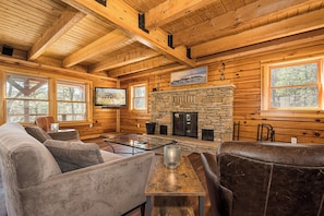A log cabin interior with a stone fireplace, wooden walls, and a television mounted above it.
