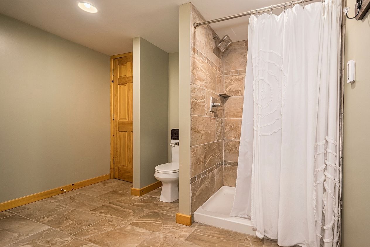 Un baño con ducha, inodoro y puerta de madera.