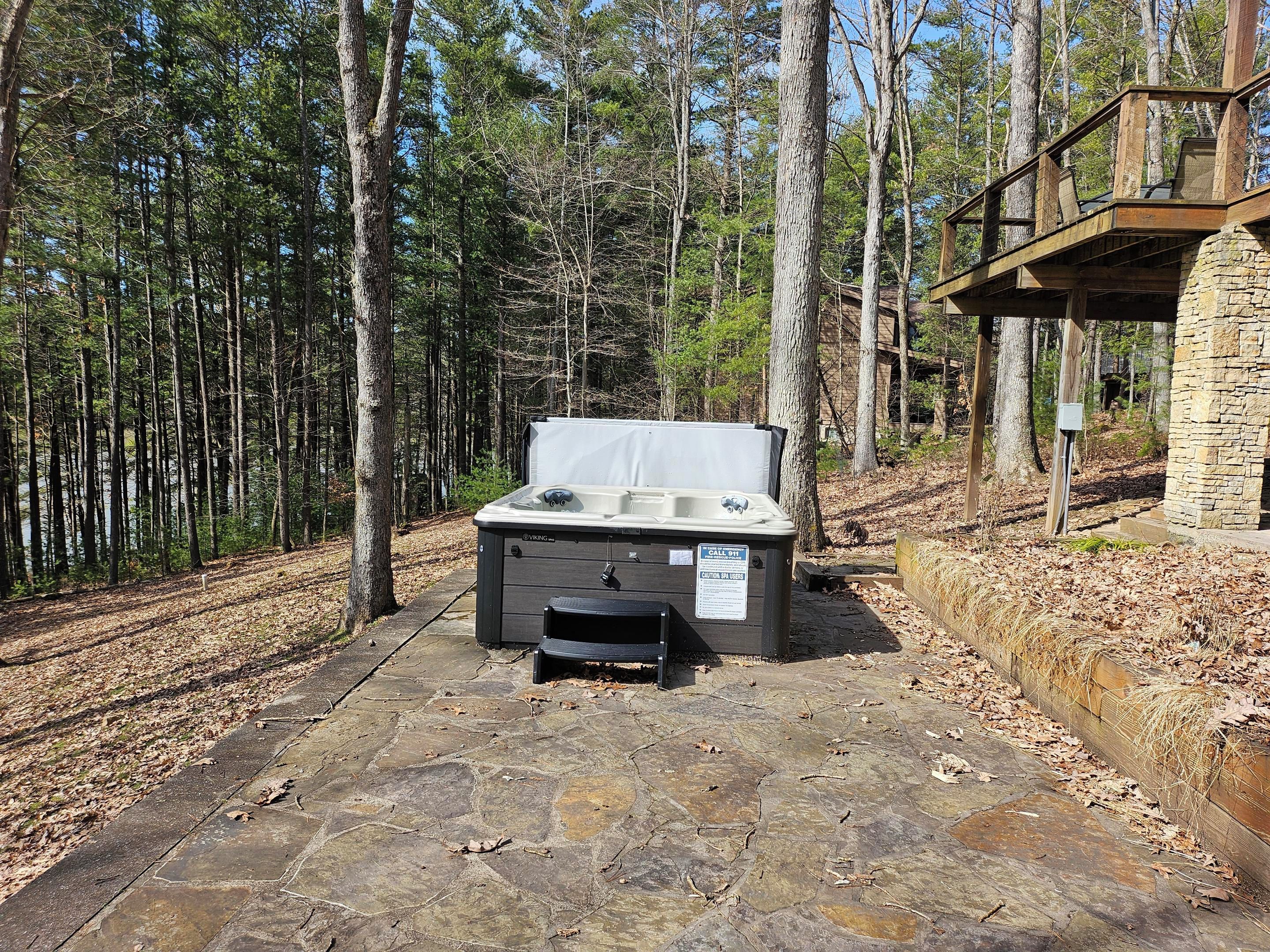 An outdoor hot tub in a wooded area with a stone pathway and a wooden deck.