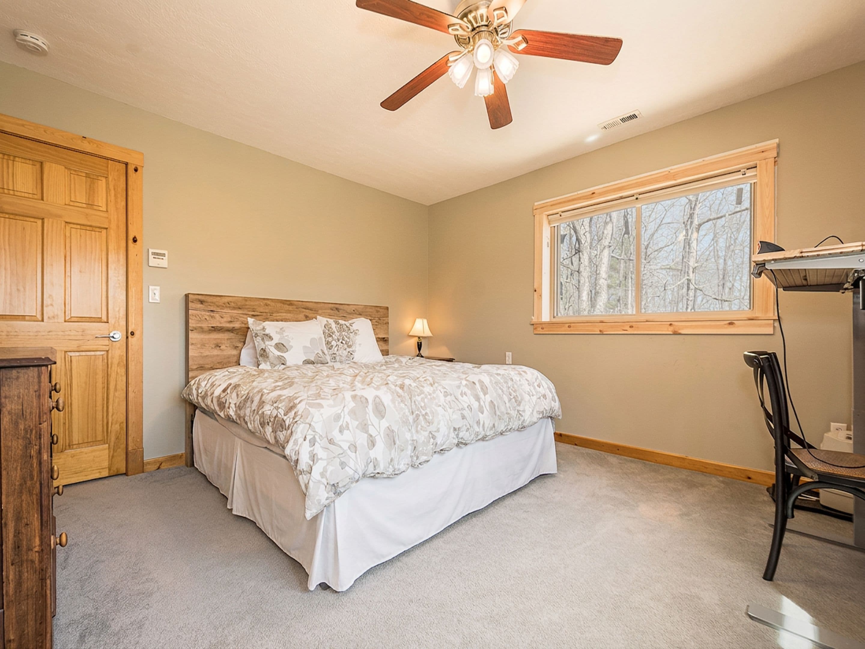 A bedroom with a bed, a ceiling fan, a window, and a wooden door.
