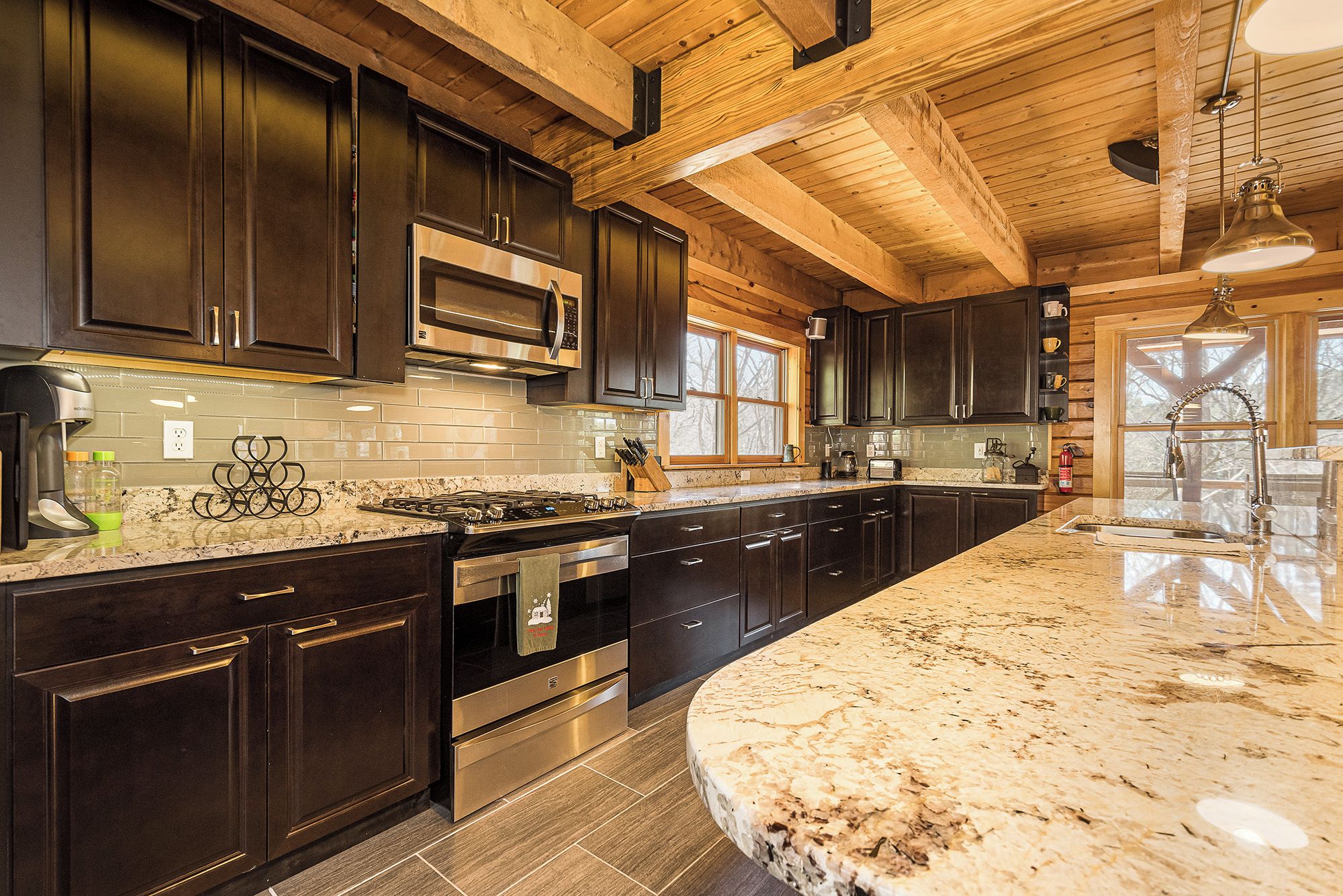 A modern kitchen with dark wood cabinets, stainless steel appliances, and a large granite island.