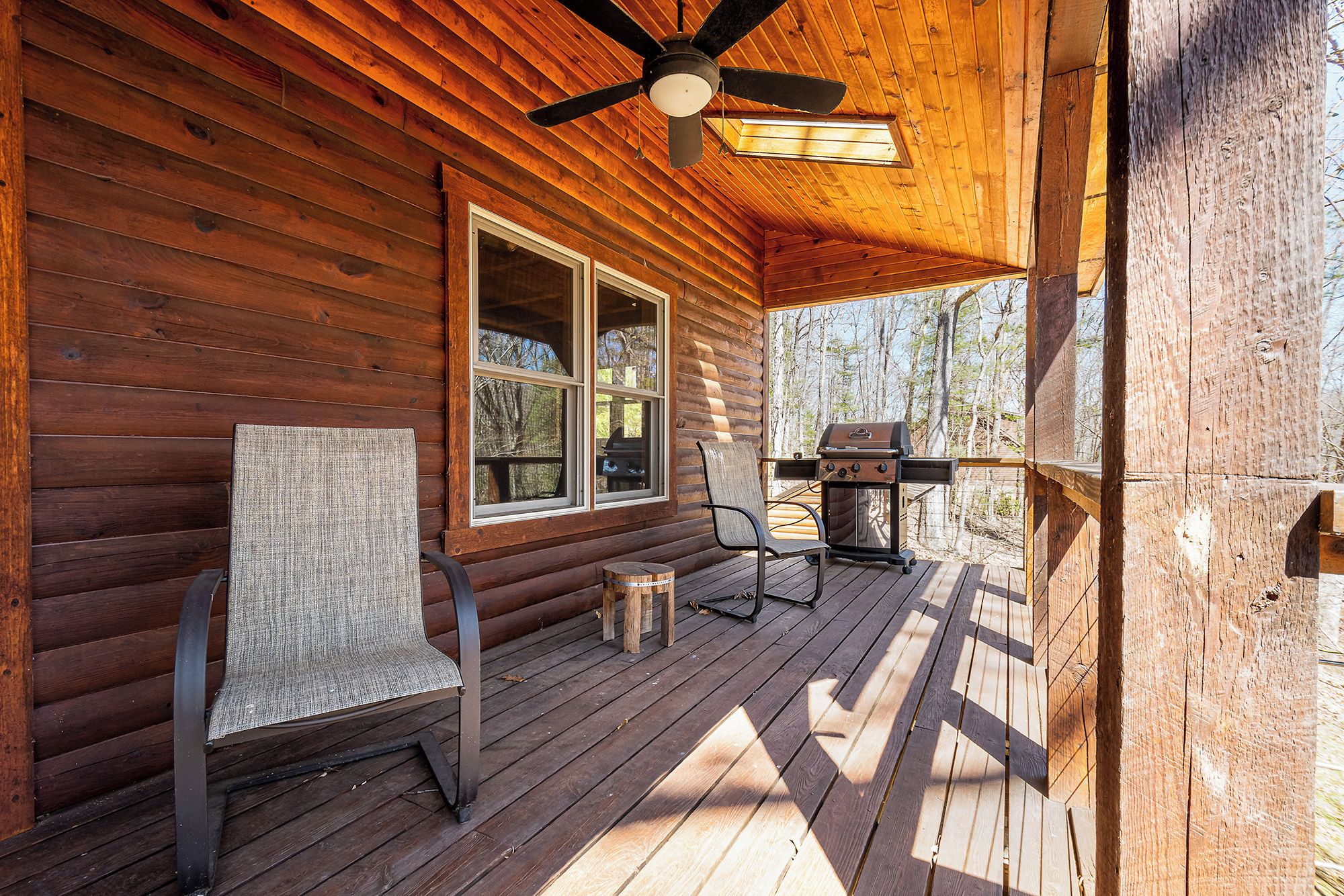A wooden cabin with a porch, a ceiling fan, a grill, and a chair.