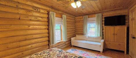 Una habitación tipo cabaña de madera con una cama, un sofá, un televisor y un ventilador de techo.