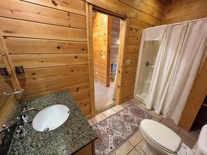 Baño de cabaña de madera con lavamanos, inodoro y ducha de granito.