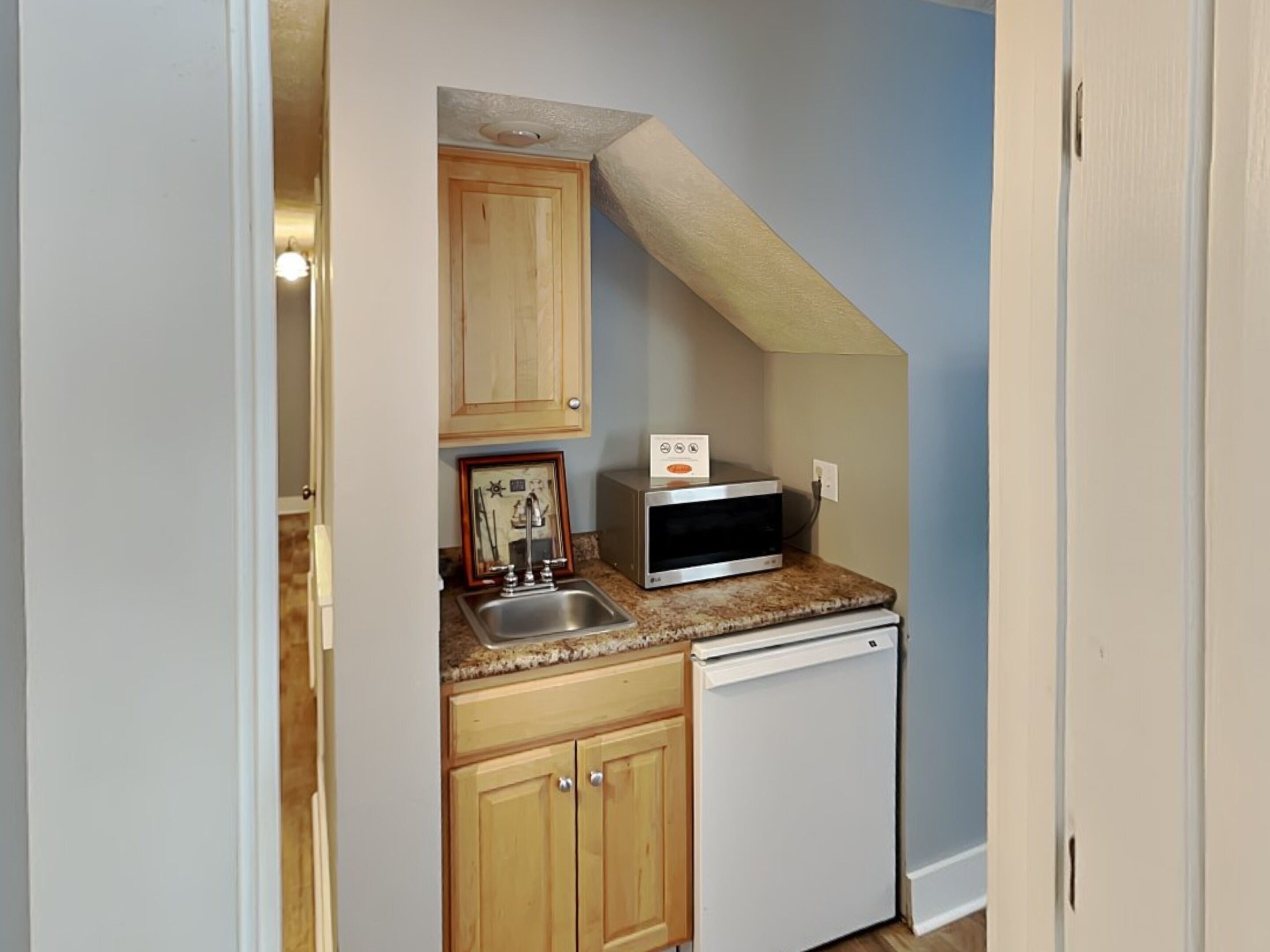 A compact kitchen with wooden cabinets, a stainless steel sink, a microwave, and a white dishwasher.