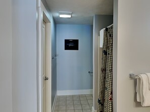 Ein schmaler Korridor mit hellblau gestrichener Wand, einer Tür links und einem Duschbereich rechts.