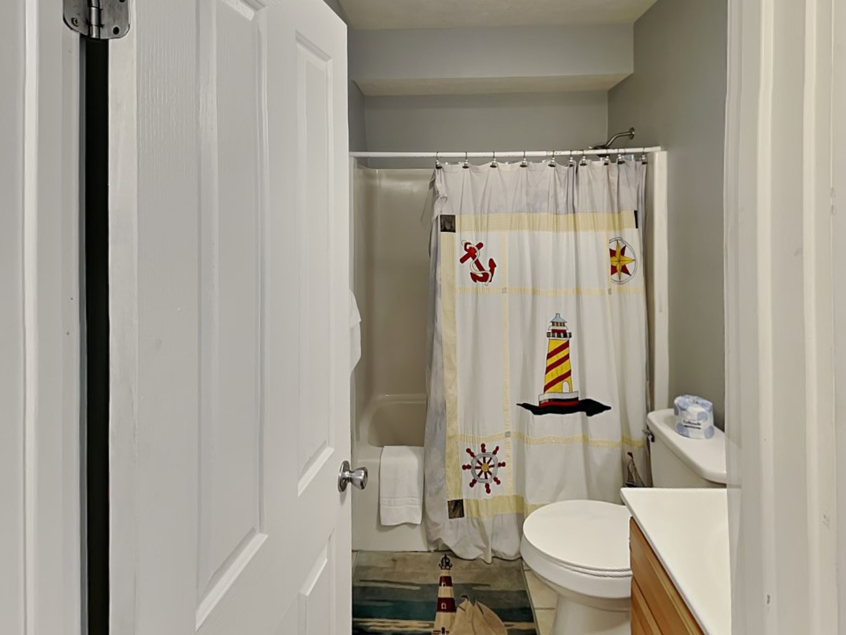 Ein Badezimmer mit weißer Tür, Toilette und einer Duschvorhang mit nautischen Motiven.