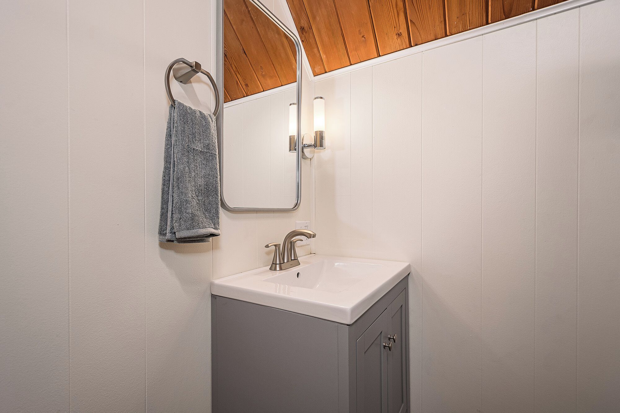 A bathroom with a white sink, a mirror, and a towel hanging on a metal towel ring.