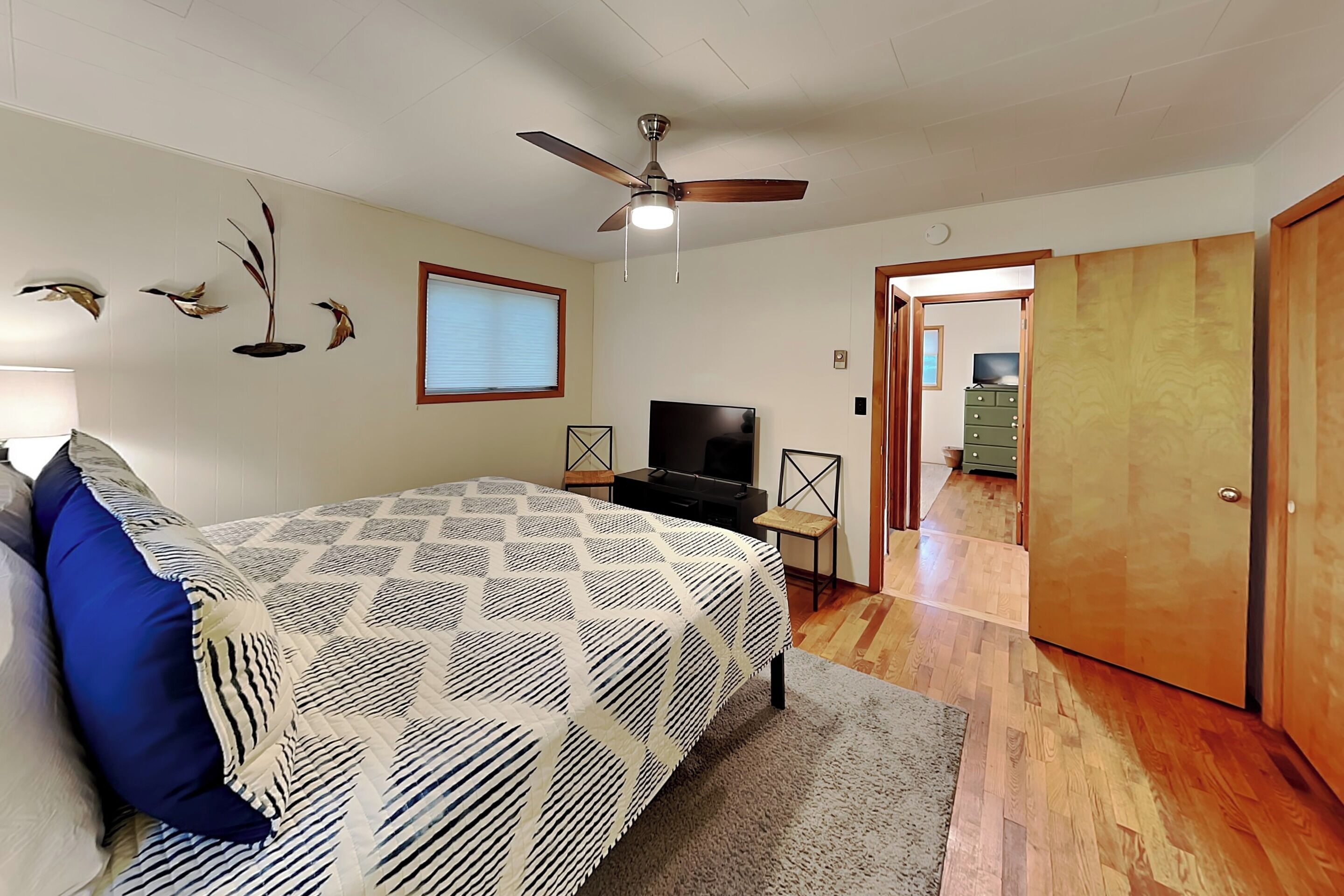 A bedroom with a bed, a ceiling fan, a TV, and a wooden door.