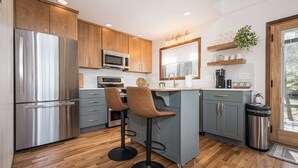 A modern kitchen with a stainless steel refrigerator, a microwave, and a coffee maker. There are two bar stools and a sink with a faucet. - Blue Horizon by Taylor Made Deep Creek (Swanton)