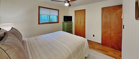 Un dormitorio con cama, ventilador de techo, ventana, cómoda y dos puertas.