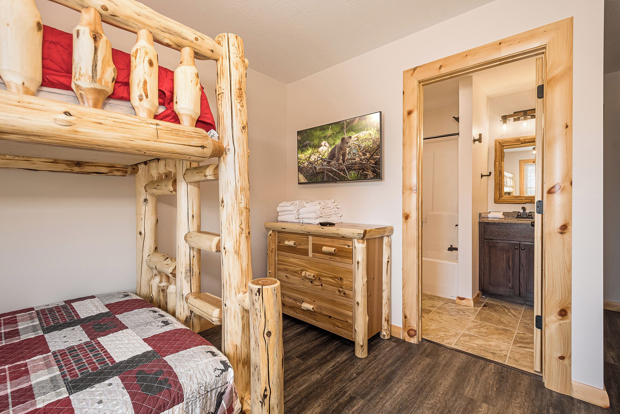 Une pièce avec un lit superposé, une commode en bois, un tableau et une salle de bain visible à travers une porte ouverte.
