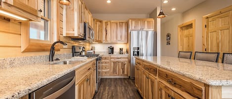 A modern kitchen with wooden cabinets, granite countertops, stainless steel appliances, and pendant lighting.