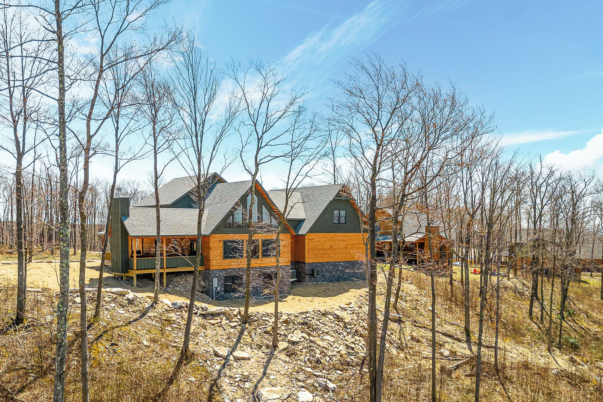 A cabin with a wooden exterior, a stone foundation, and a sloped roof, surrounded by trees and a clear sky.