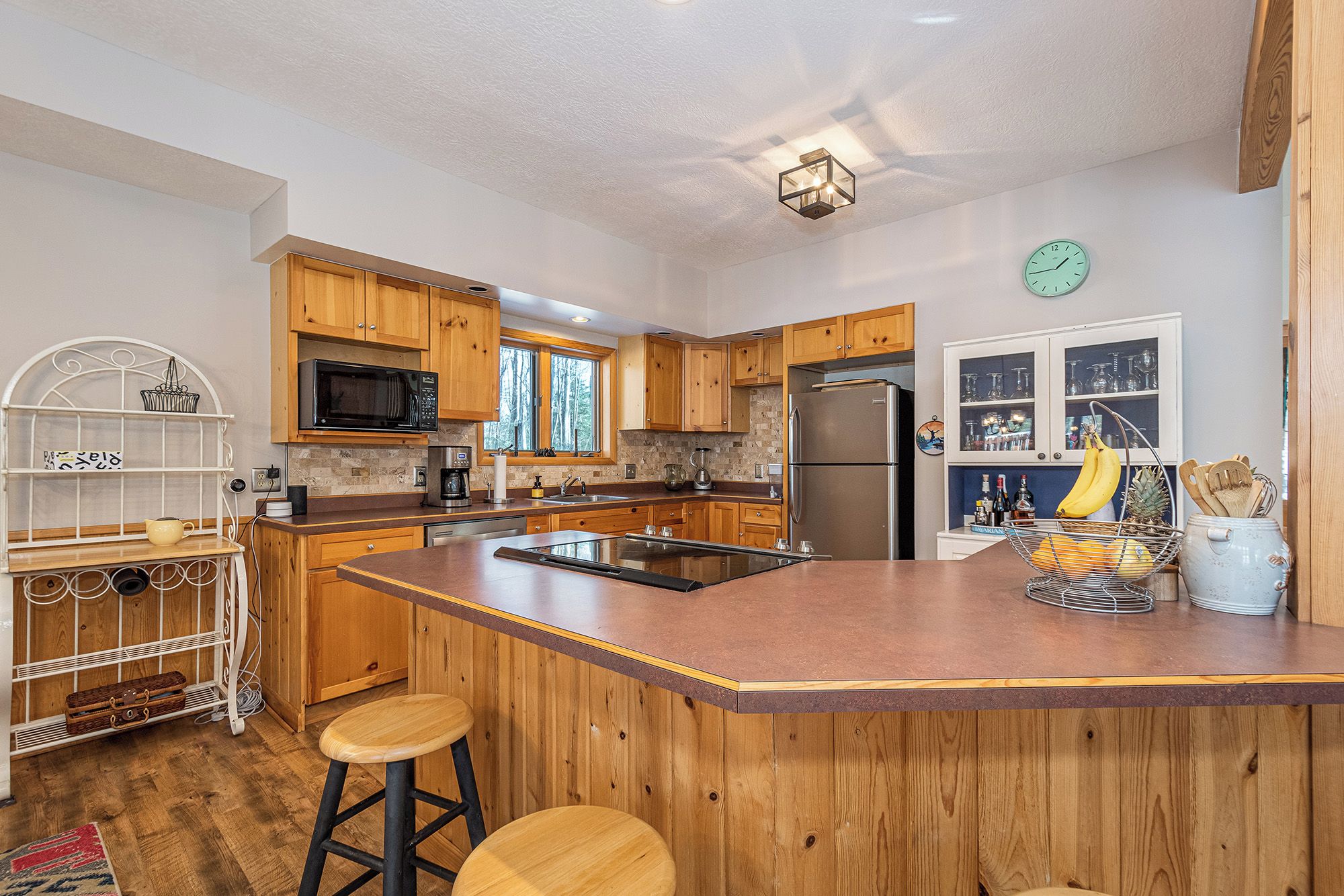 A kitchen with wooden cabinets, a stainless steel refrigerator, and a large island with stools.