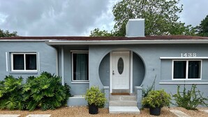 A single-story house with a gray facade, a white door, and the number 1438 on the right side. - Centrally located 5 bedroom house with parking (Miami)