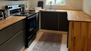 A modern kitchen with dark cabinets, a wooden countertop, a stove, and a window providing natural light. - Centrally located 5 bedroom house with parking (Miami)