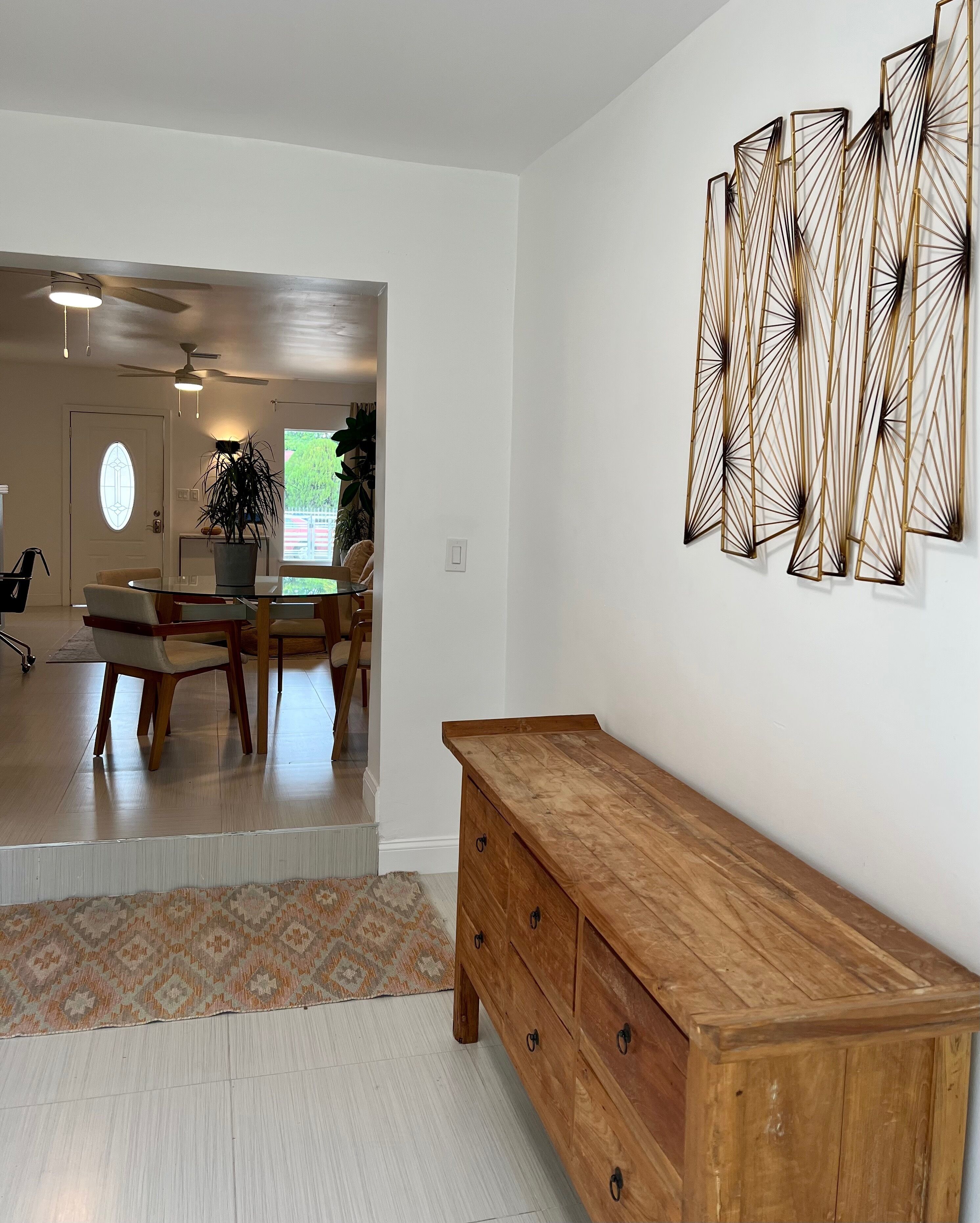 Una sala de estar moderna con un aparador de madera, un comedor con mesa de vidrio y un elemento decorativo en la pared.