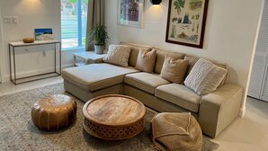 A living room with a sectional sofa, a round wooden coffee table, a leather pouf, and a small side table with a bowl. - Centrally located 5 bedroom house with parking (Miami)