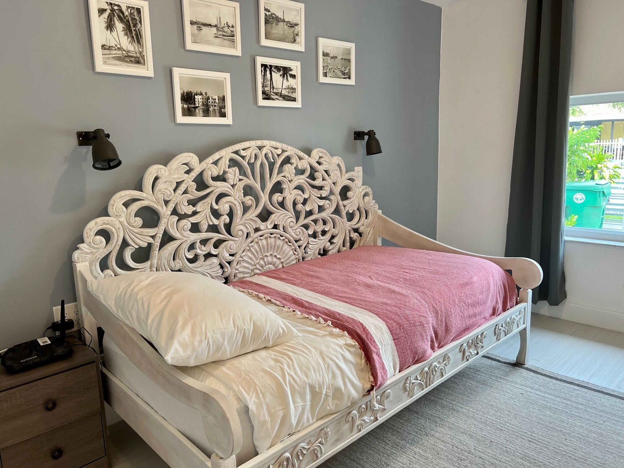 Un dormitorio con una cama blanca ornamentada, una pared gris y apliques de pared negros.
